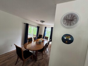A dining room with a wooden table and chairs, a chandelier, and a clock on the wall.