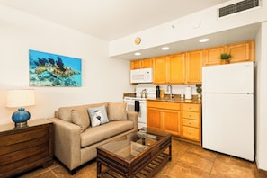 A compact living space with a kitchenette, a sofa, a coffee table, and a painting on the wall. - Tropical Kahana Hideaway with Ocean Views (Lahaina)