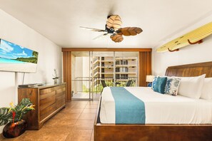 A hotel room with a bed, a ceiling fan, a surfboard, a view of a balcony, and a plant. - Tropical Kahana Hideaway with Ocean Views (Lahaina)