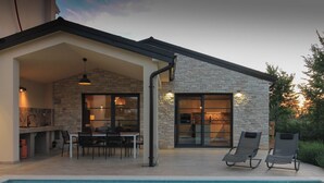 Uma casa moderna com piscina, apresentando uma área de refeições, cozinha e duas cadeiras de descanso à beira da piscina.