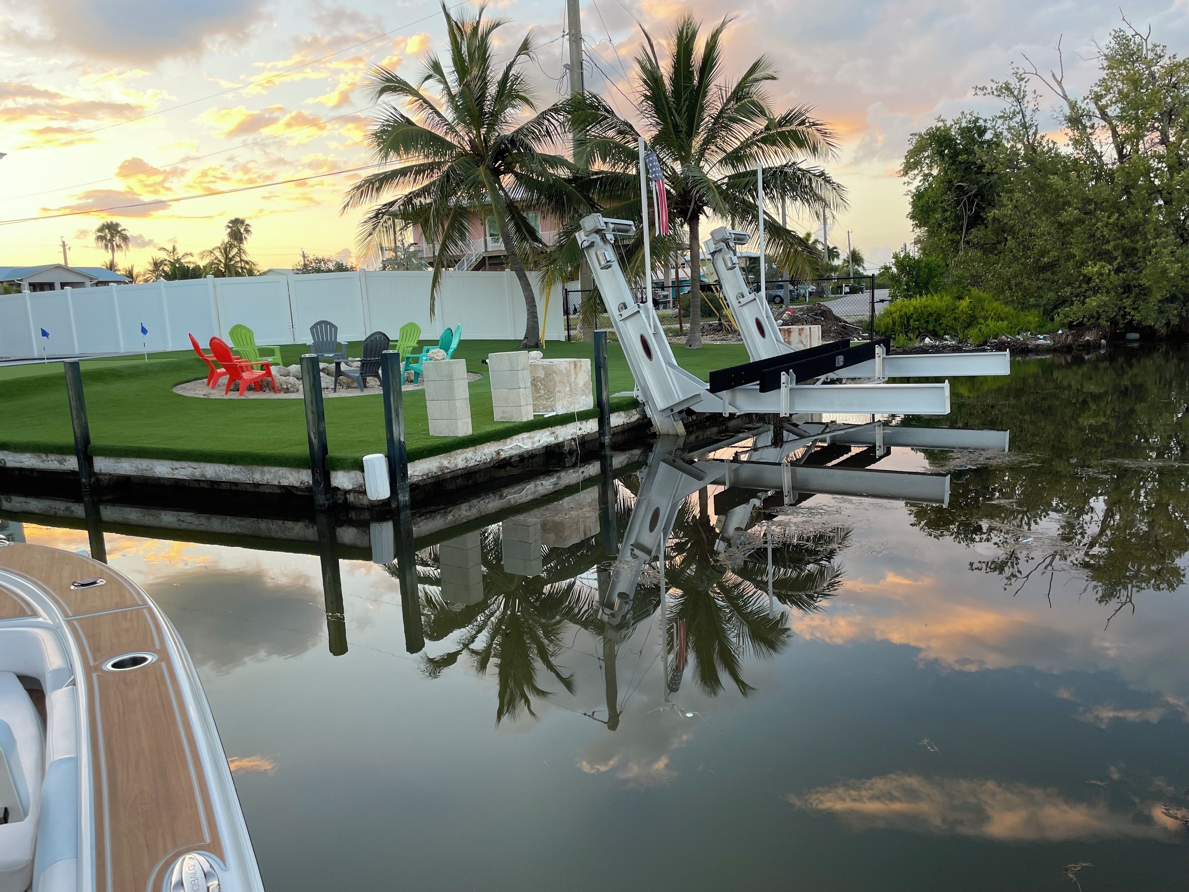 A marina with a dock, a grassy area with chairs, and palm trees.