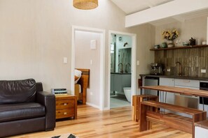 Cozy living space with a sofa, nightstand, and wooden bench, leading to a bathroom and kitchen area.