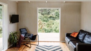 Una sala de estar moderna con un sofá de cuero negro, una butaca negra, un ventanal con vistas a la vegetación y un televisor montado en la pared.