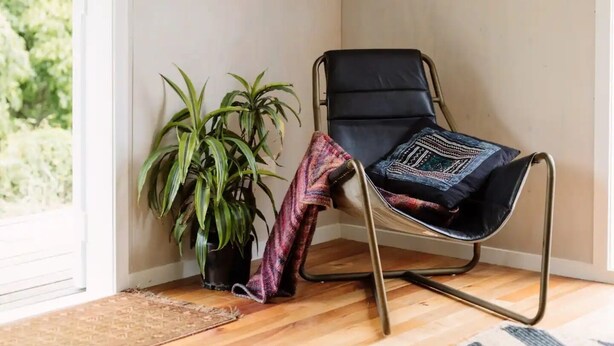 A room with a black leather chair, a potted plant, and a flat-screen TV mounted on the wall. - Wainui Stream Cottage (Raglan)