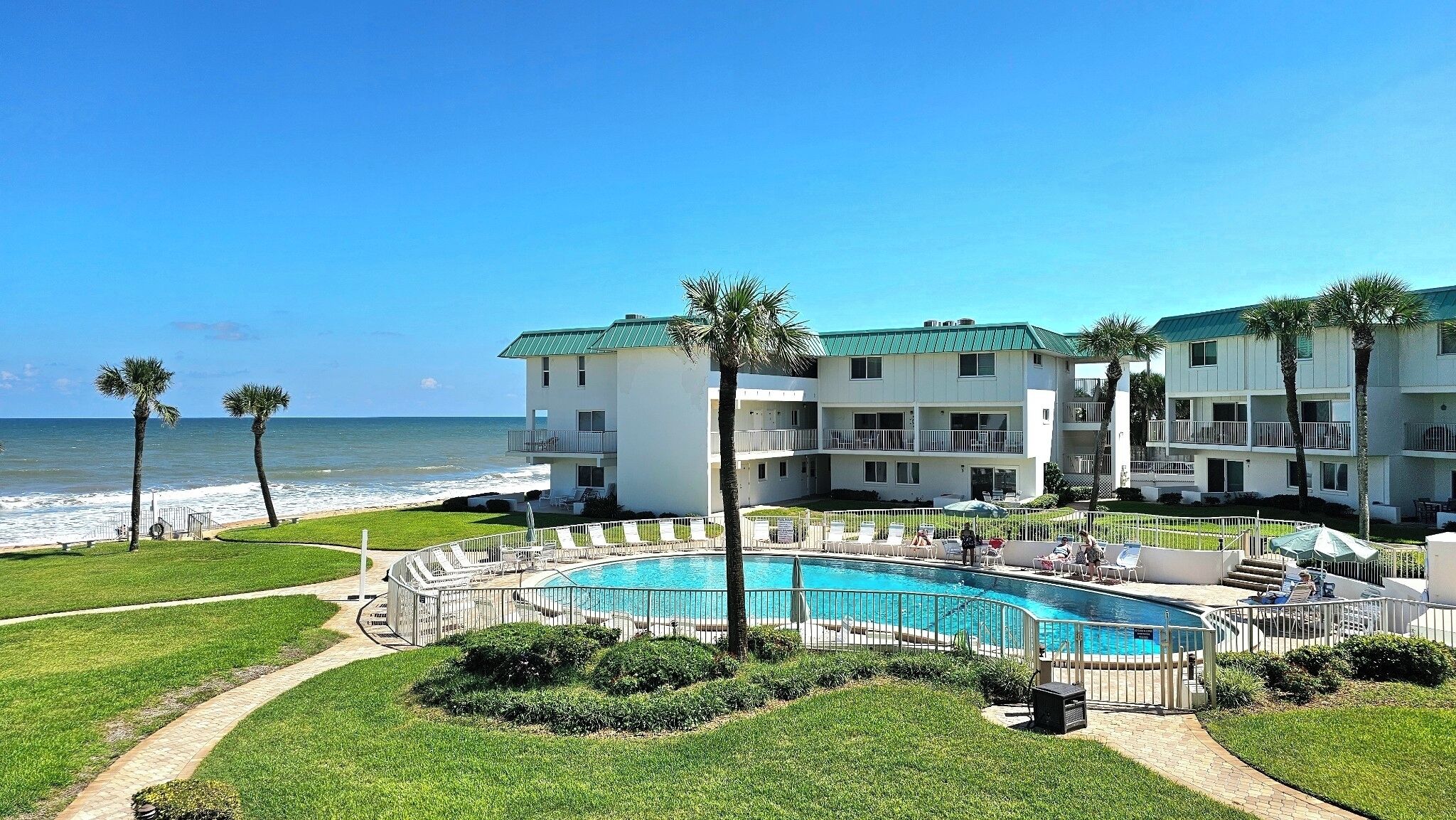 A beachfront hotel with a swimming pool, palm trees, and ocean views.