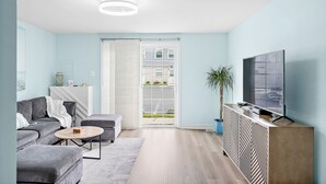 Un salon moderne avec un canapé gris, une table basse ronde et un téléviseur posé sur une console en bois.