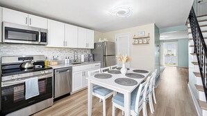 Une cuisine moderne équipée d’appareils électroménagers en acier inoxydable, un coin repas avec une table et des chaises blanches, et un escalier menant à un autre niveau.