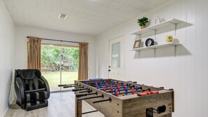 A room with a foosball table, a massage chair, and a sliding glass door leading to a garden. - Spacious house with massage chair and game room (Beaumont)