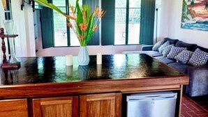A modern kitchen with a wooden island, a refrigerator, and a dining area with a sofa and patterned cushions. - Pacific Ocean-Front Villa de Azul. stunning Sunrises & Sunsets, 3bd 2 full baths (Provincia de Puntarenas)