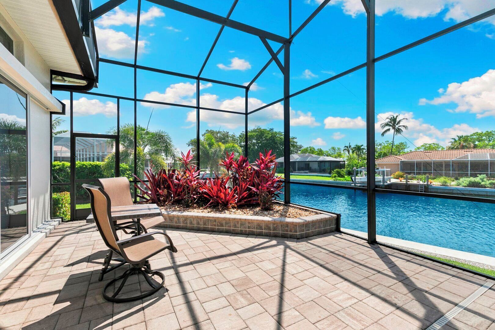 A patio with a pool, a chair, and red plants.