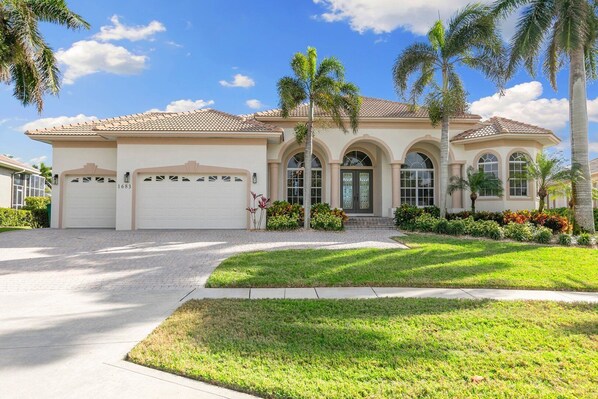 A two-story house with a tiled roof, a front garage, and a well-maintained lawn with palm trees. - This waterfront home on Marco Island is the perfect vacation destination for families or groups. (Marco Island)