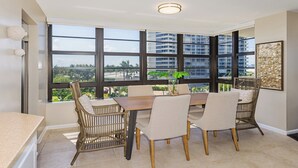 A dining area with a large window, wicker chairs, a wooden table, and a view of a cityscape.