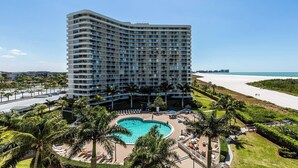 A high-rise hotel with a pool area, palm trees, and a beach view.