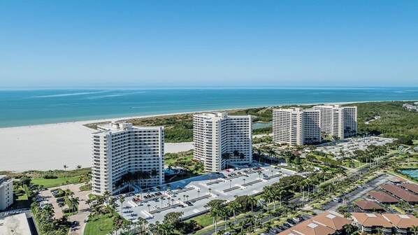A coastal hotel complex with three high-rise buildings, a parking area, and a beach in the background.