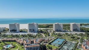 Un resort con varios edificios altos, una playa y un complejo de canchas de tenis.