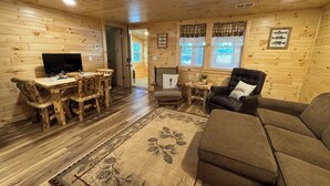 Interior de una cabaña de madera con una mesa de comedor, sillas, un sofá y un televisor.