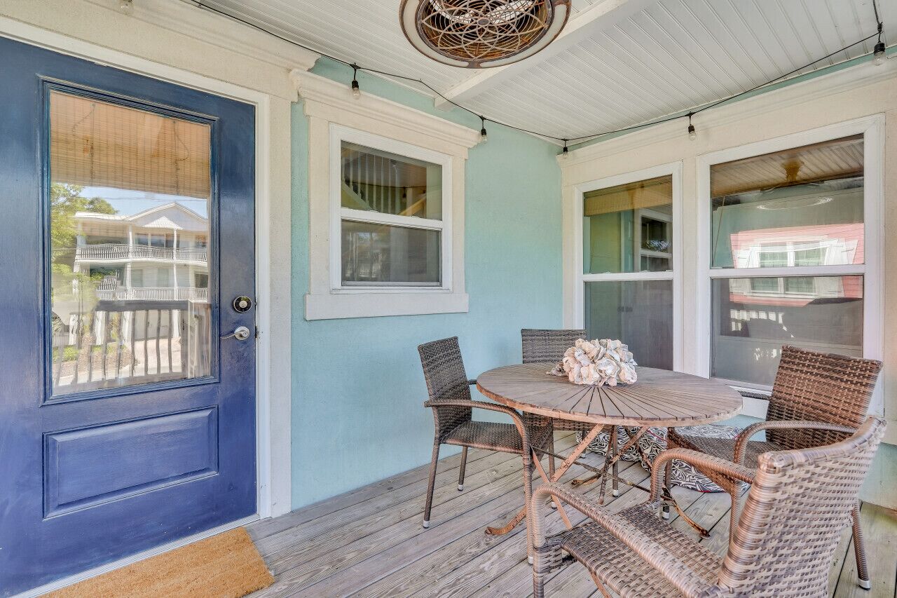 A porch with a blue door, wicker furniture, and a small table with a vase.