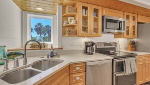 Een moderne keuken met houten kastjes, roestvrijstalen apparatuur en een groot raam met uitzicht op palmbomen.