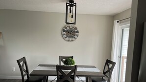 A dining area with a rectangular table, four chairs, a potted plant, a wall clock, and a pendant light fixture. - Upper level home in Grande Prairie (Grande Prairie)
