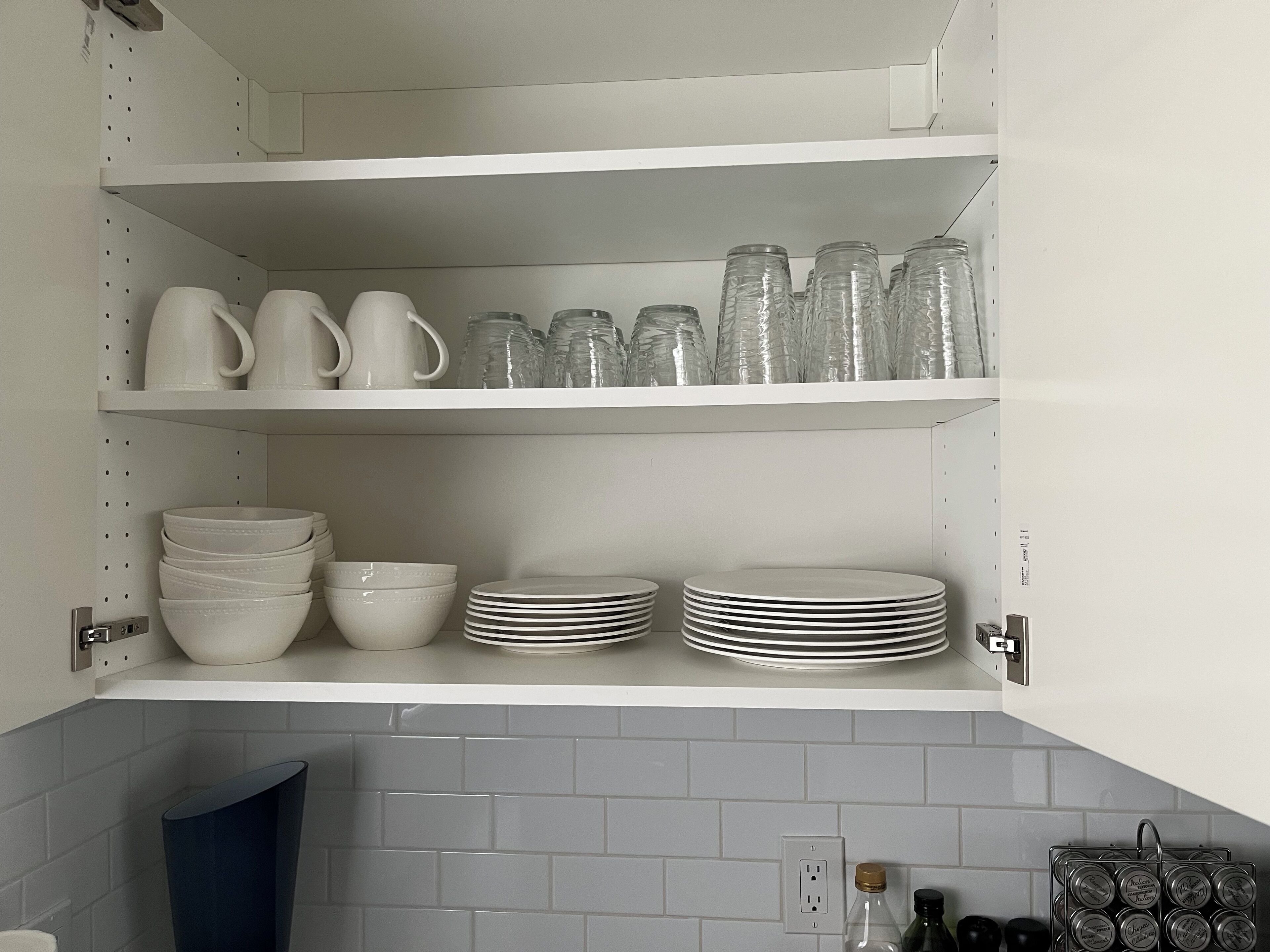 Una cocina con armarios blancos, estantes que exhiben vajilla, cuencos y cristalería.