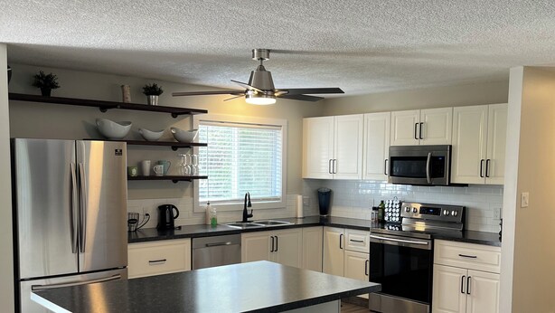 A modern kitchen with white cabinets, stainless steel appliances, and a central island with stools. - Upper level home in Grande Prairie (Grande Prairie)