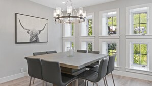 A dining area with a large table, chairs, a chandelier, and a bull-themed artwork on the wall. - Platinum-rated 2 Bedroom ski in, ski out Condo in BC Village (Avon)