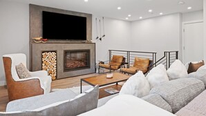 A modern living room with a fireplace, seating area, and a flat-screen TV mounted above it. - Platinum-rated 2 Bedroom ski in, ski out Condo in BC Village (Avon)