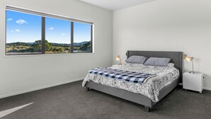 A bedroom with a large window, a bed with a patterned bedspread, a ceiling fan, and bedside lamps.