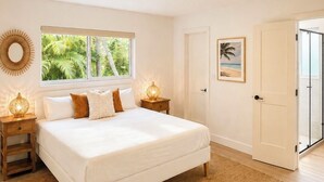 Une chambre à coucher avec un lit, une fenêtre donnant sur un espace verdoyant, une porte et un luminaire fixé au mur.