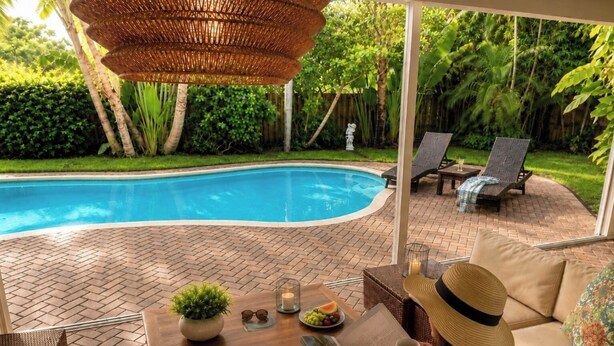 Un espace aménagé au bord de la piscine, avec un canapé, une table agrémentée d’une plante et une vue sur la piscine.