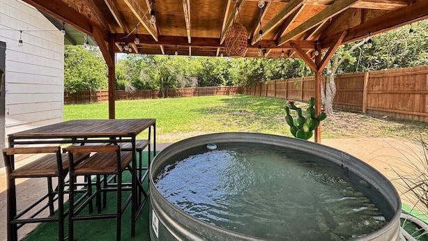 Et overdækket udendørs område med jacuzzi, træbord og stole.