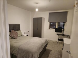 A bedroom with a bed, a wardrobe, a radiator, a window with a TV, and a door. - Luxurious 2-bed Haven in the Heart of Barking (Barking)