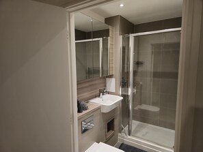 A modern bathroom with a glass-enclosed shower, a sink with a mirror, and a towel rack. - Luxurious 2-bed Haven in the Heart of Barking (Barking)