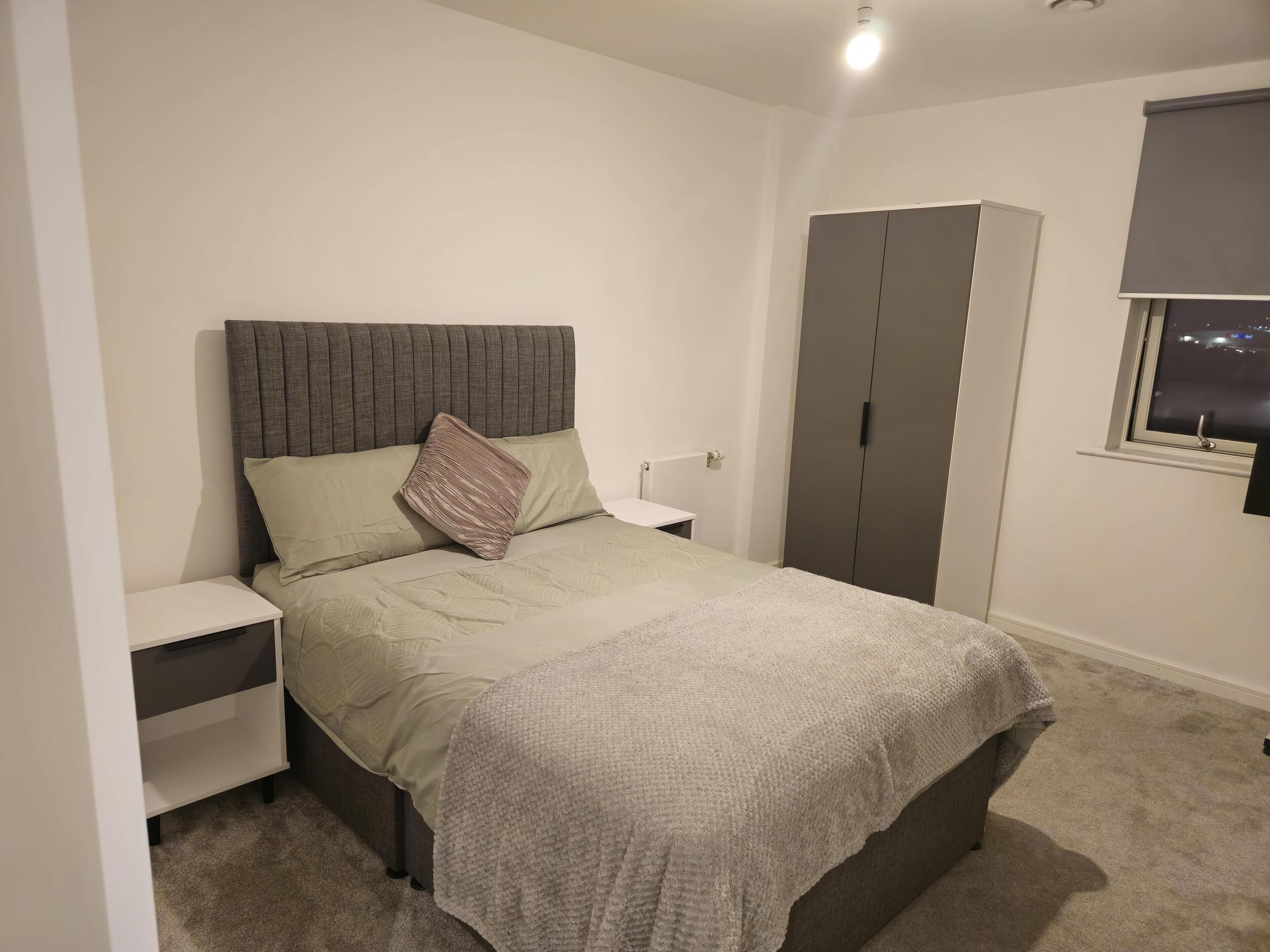 A bedroom with a bed, a wardrobe, a nightstand, and a window with a view of the night sky.