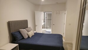 Une chambre à coucher comprenant un lit, une table de chevet et une porte donnant sur une salle de bain.