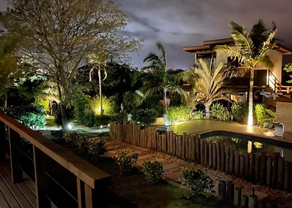 Vista noturna de um resort com piscina, deck de madeira e paisagem tropical.