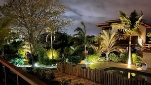 A nighttime view of a resort with a pool, wooden deck, and tropical landscaping.