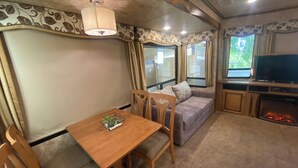 Un intérieur de camping-car accueillant, avec une table à manger, des chaises, un canapé, un téléviseur et une cheminée.