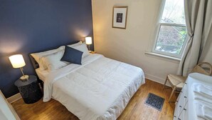 Un dormitorio con cama, dos lámparas de noche, una ventana con cortinas, una silla y un aparador.