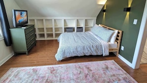 A bedroom with a bed, a TV, a ceiling fan, and built-in shelving.