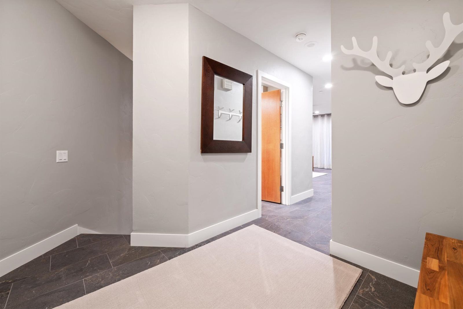 A hallway with a framed mirror, a rug, and a deer head decoration.