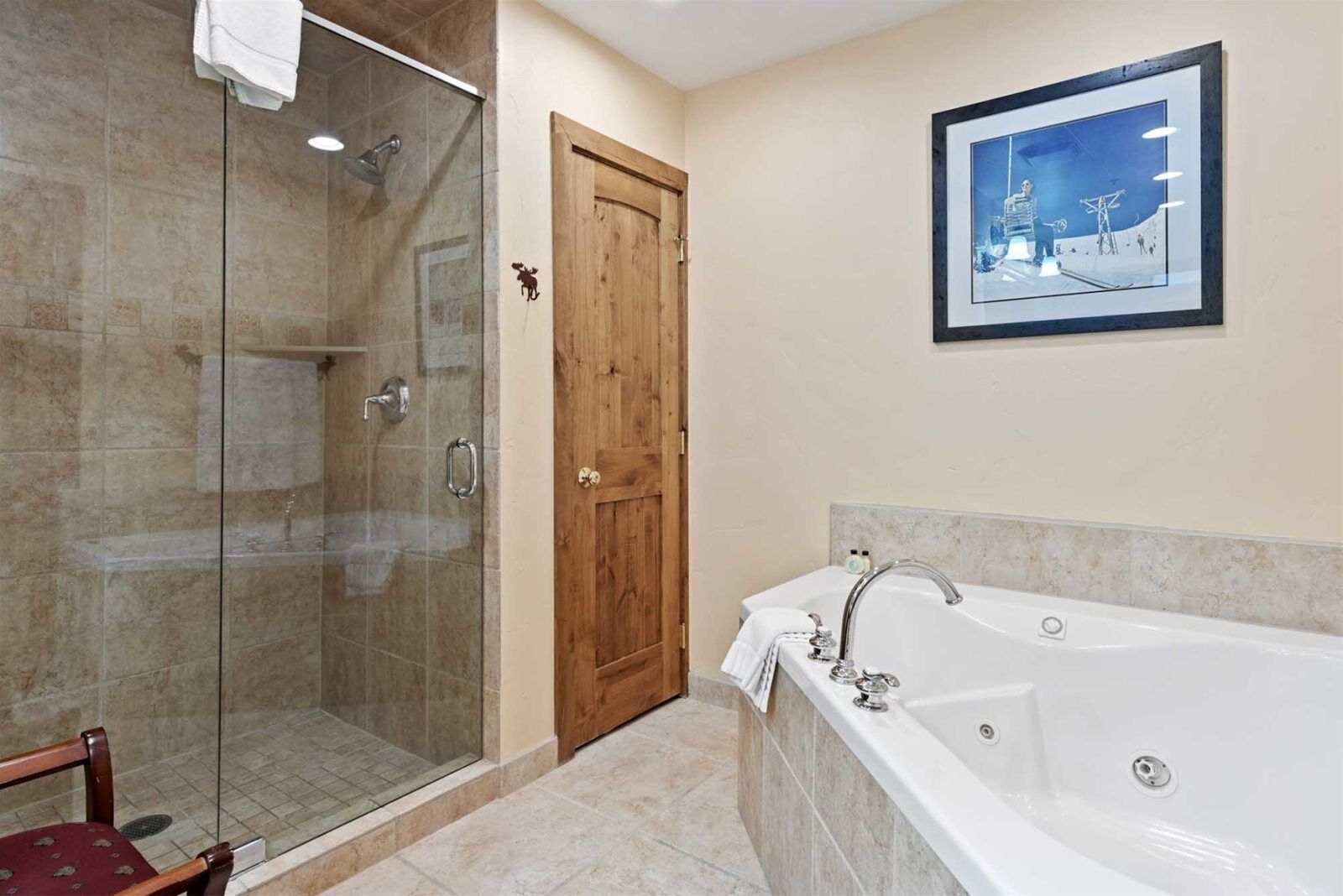 A bathroom with a glass-enclosed shower, a wooden door, a large bathtub, and a framed picture on the wall.