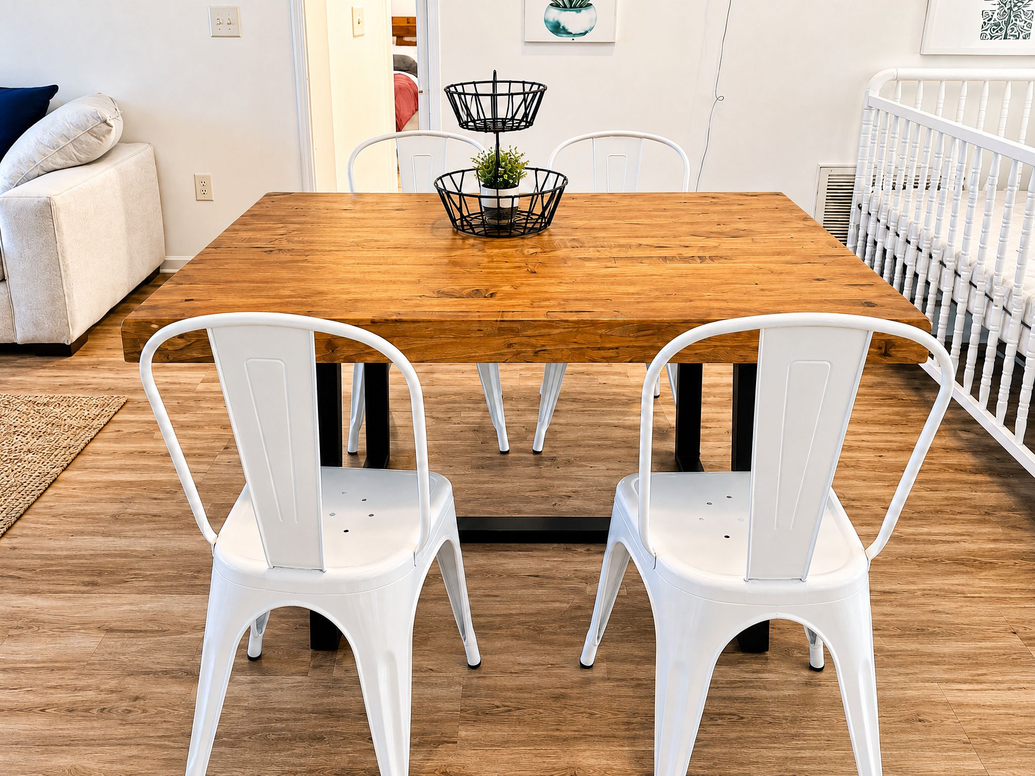 Un área de comedor con una mesa de madera, dos sillas blancas y un atril para planta negro.