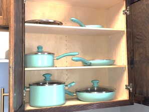 Eine Küchenschrank mit drei Einlegeböden, auf jedem ein Topf und eine Pfanne.