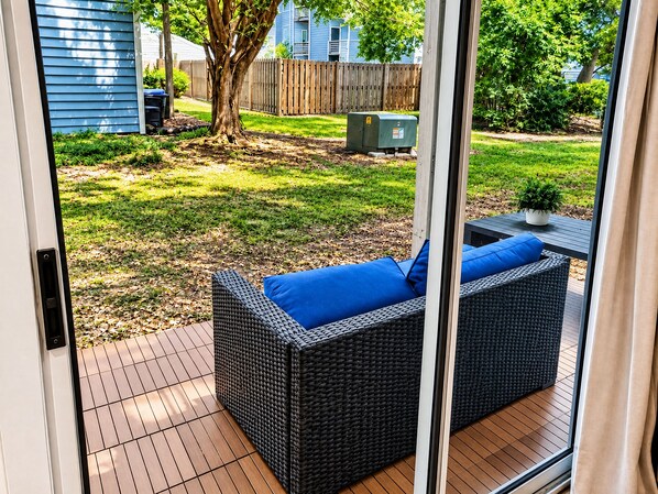 Eine Terrasse mit einem Korbsessel, Kissen, einem kleinen Tisch und einem Blumentopf.