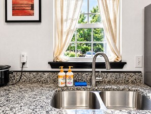 A kitchen with a double sink, granite countertop, and a window with curtains.