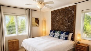 Una camera da letto con un letto, una ventola a soffitto, un comodino con una lampada, un quadro appeso al muro e una finestra con persiane.