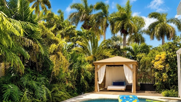 Una piscina con un lettino galleggiante, circondata da una rigogliosa vegetazione tropicale e un gazebo.