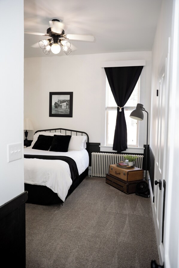 A bedroom with a bed, a radiator, a window with curtains, a ceiling fan, and a picture on the wall. - The Loft on the Square (Highland)