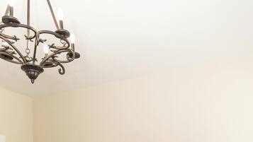 A bedroom with a bed, a chandelier, a nightstand, a lamp, and a wall art piece.